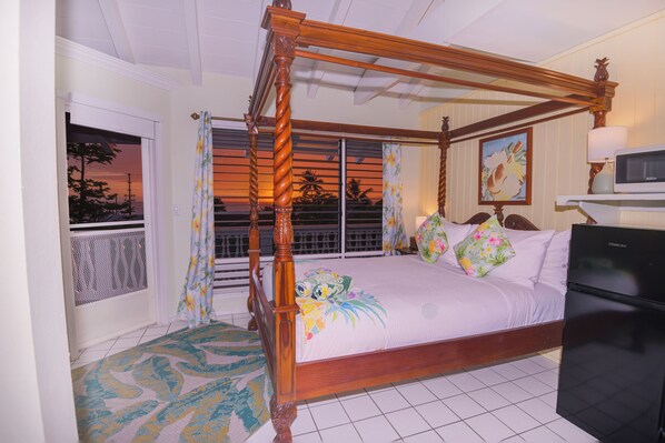 A four-poster bed with a floral bedspread and pillows, a television, and a refrigerator in a hotel room. - Big Island Retreat (Kailua-Kona)