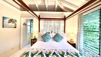 A bedroom with a bed, a nightstand, a lamp, a window with curtains, and a view of greenery outside.