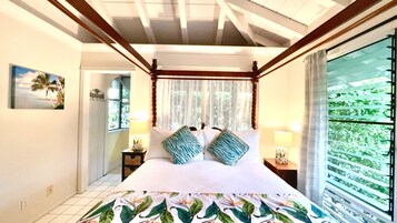 Une chambre à coucher avec un lit, une table de chevet, une lampe, une fenêtre avec des rideaux et une vue sur la verdure à l’extérieur.