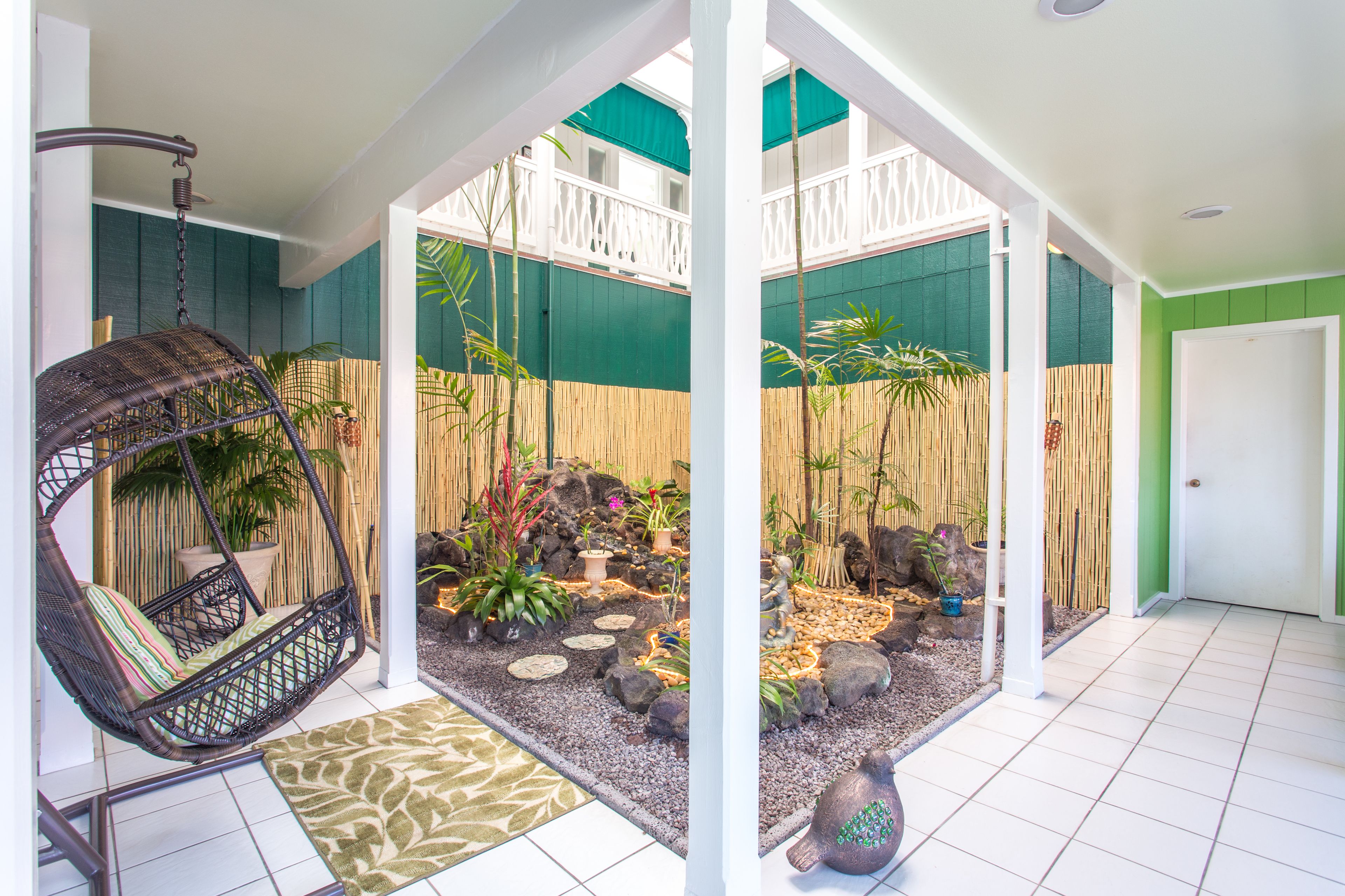 Una habitación con una hamaca colgante, un pequeño jardín con plantas y rocas, y una puerta blanca.