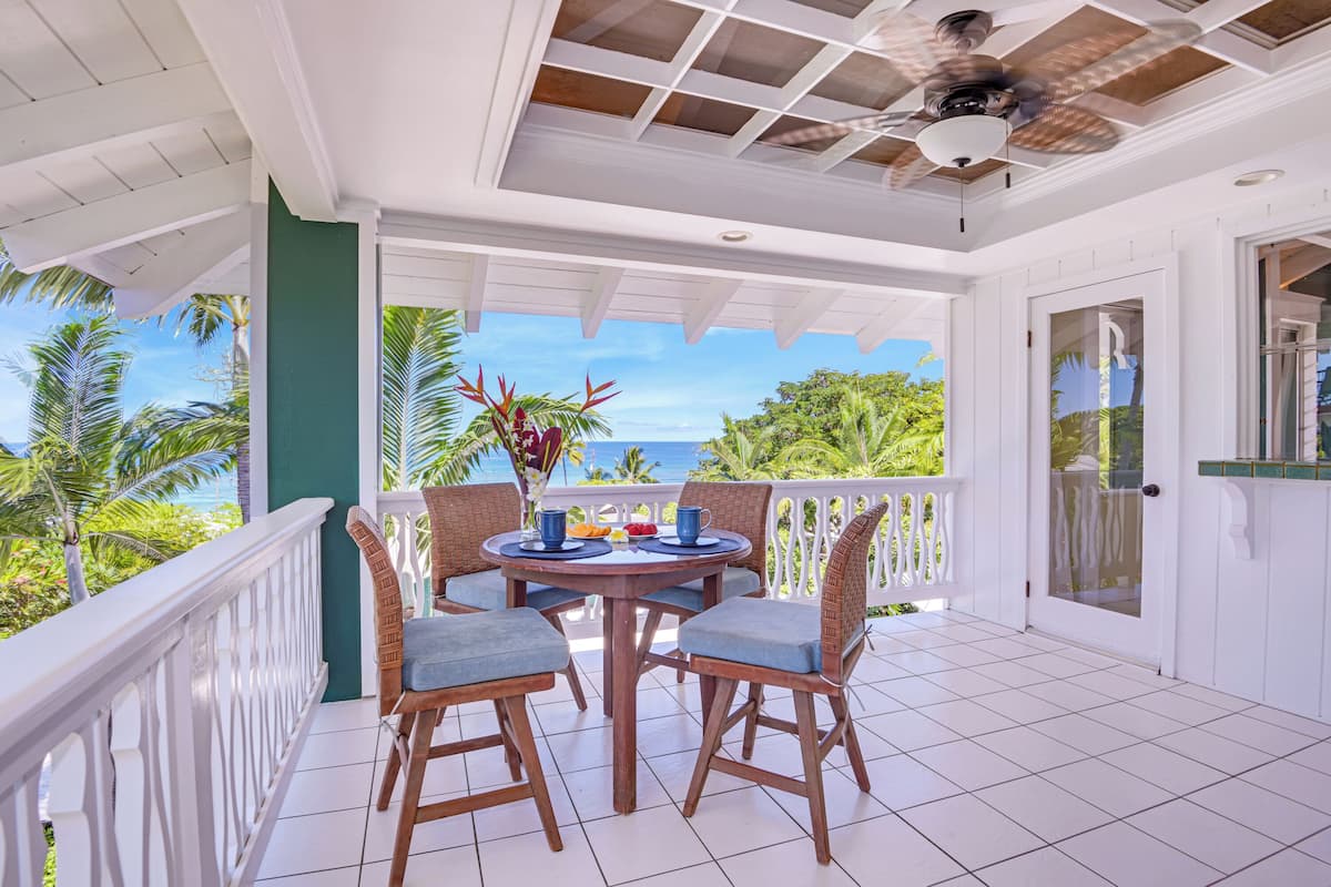 A covered outdoor area with a table and chairs, a ceiling fan, and a view of the ocean.