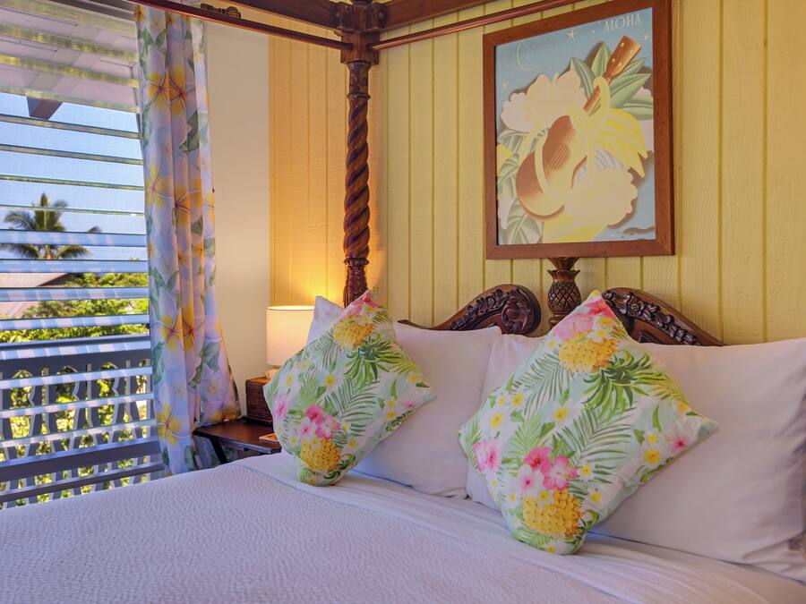 Un lit avec des coussins à motifs floraux, une tête de lit en bois et un tableau encadré accroché au mur.