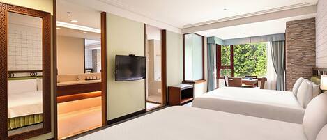 A hotel room with two beds, a TV, a desk, and a view of greenery.