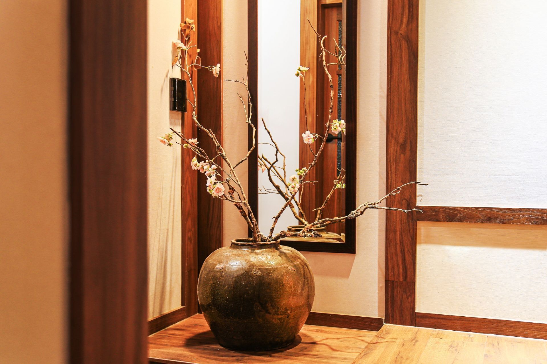 Un jarrón con ramas y flores sobre una mesa de madera en un pasillo.