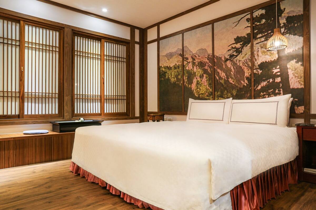 A traditional Japanese-style bedroom with tatami flooring, a large bed with white bedding, a wooden headboard, and a sliding shoji screen window.