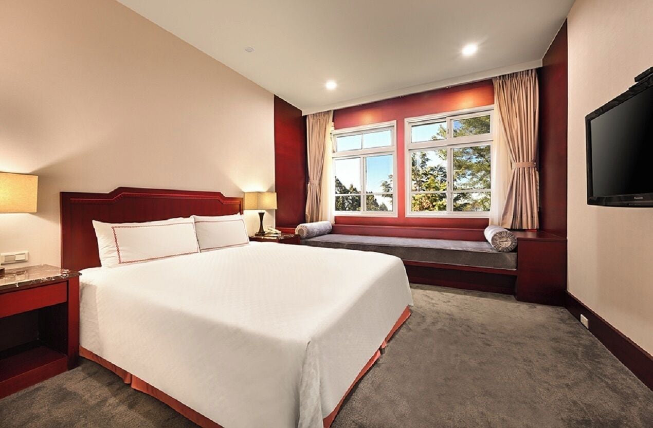 A hotel room with a large bed, a bench by the window, a TV, and a nightstand.