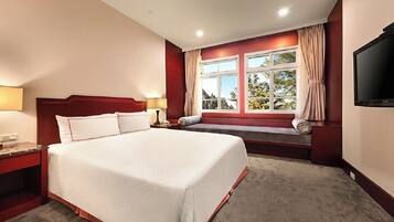 A hotel room with a large bed, a bench by the window, a TV, and a nightstand.