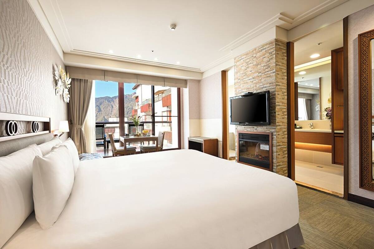 A hotel room with a large bed, a television, a fireplace, and a balcony with a view of mountains.