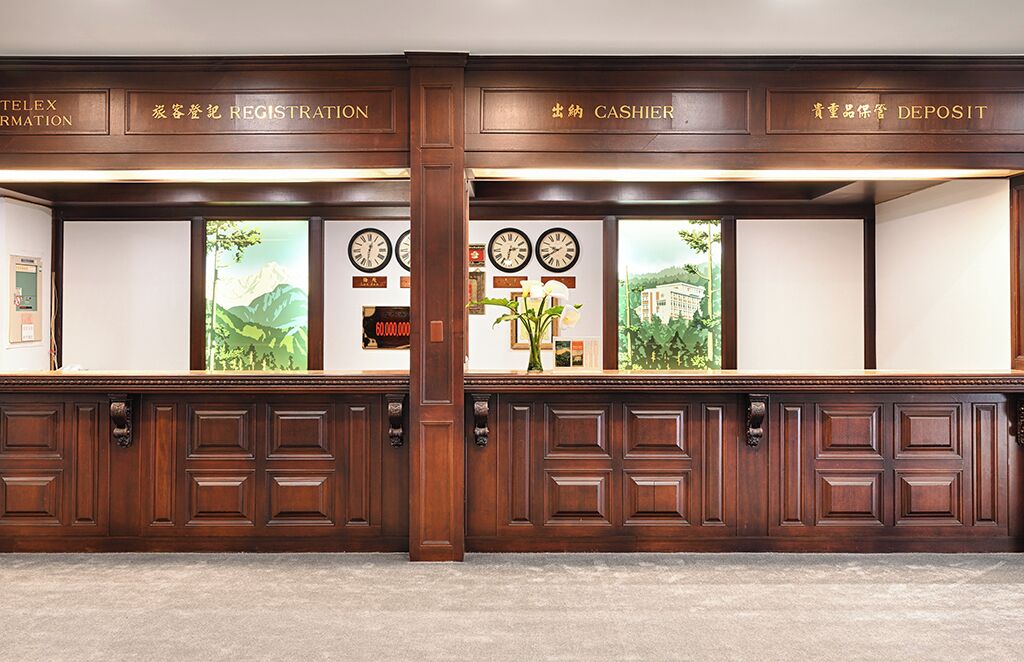 A reception desk with wooden paneling, clocks, and a floral arrangement.