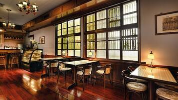 A restaurant with wooden flooring, multiple tables and chairs, large windows with bars, and hanging chandeliers.