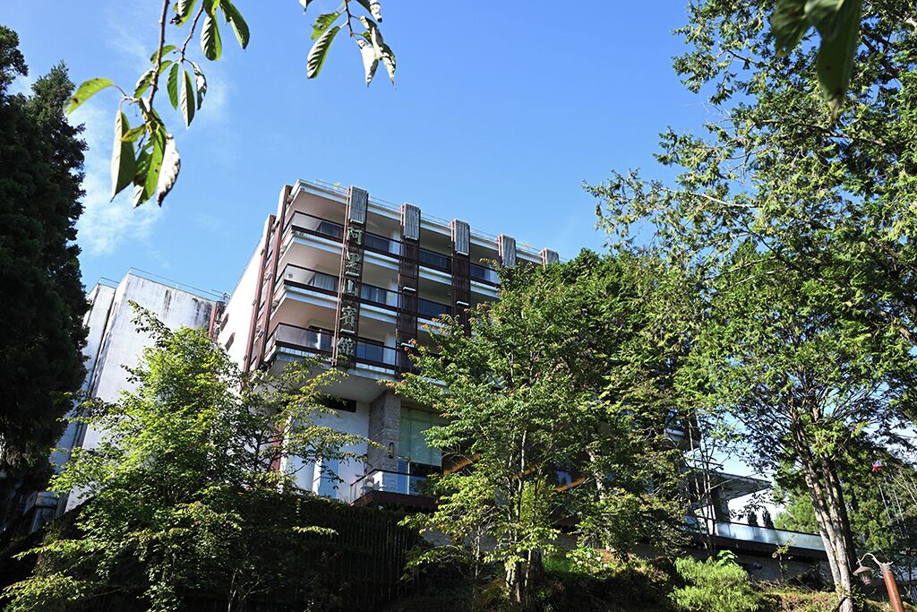 Un edificio de varios pisos con balcones, rodeado de árboles y vegetación.