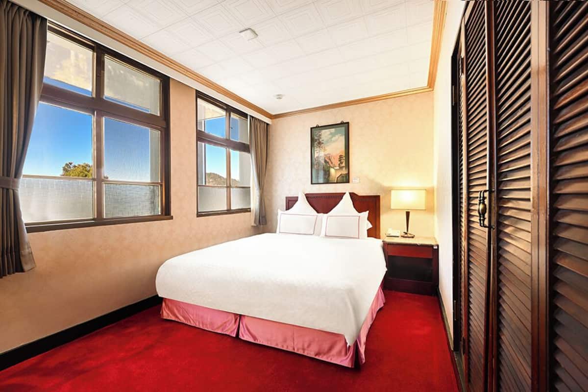A hotel room with a large bed, a nightstand, a lamp, and a window with curtains.