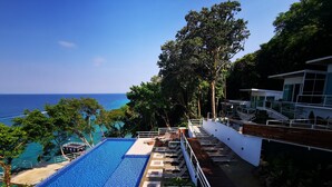 Une piscine à débordement située sur le toit, offrant une vue sur l’océan, entourée d’une végétation luxuriante et dotée d’un espace salon extérieur moderne.