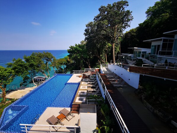 Ein Infinity-Pool auf dem Dach mit Blick auf das Meer, umgeben von üppiger Vegetation und moderner Outdoor-Sitzgelegenheit.