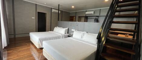 A hotel room with two beds, a ceiling fan, wooden flooring, a staircase, and a view of the outside.