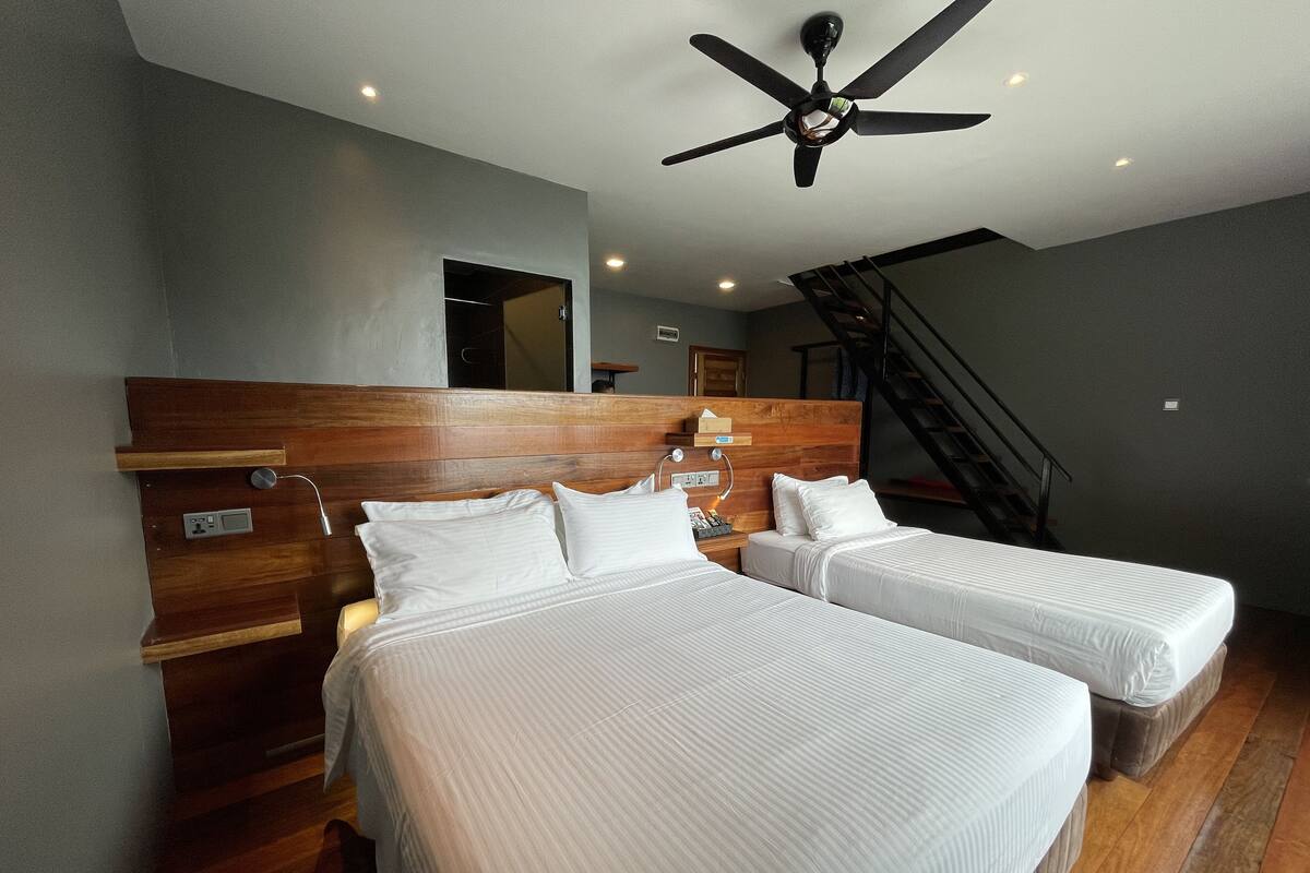 A hotel room with two beds, wooden headboard, ceiling fan, and a staircase.