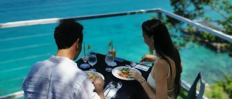 Una pareja cenando en una mesa al aire libre con vista al océano.