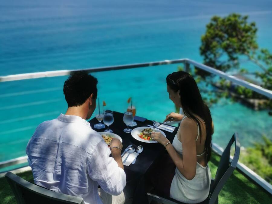 Una pareja cenando en una mesa al aire libre con vista al océano.