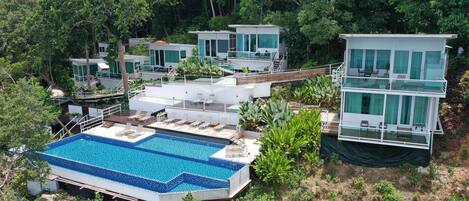 Un resort moderno con varias villas para huéspedes, una gran piscina y exuberante vegetación que rodea la propiedad.