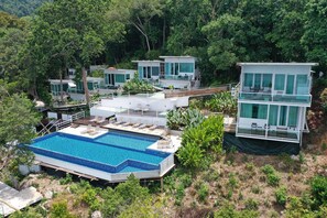 Un complexe hôtelier moderne doté de plusieurs villas pour les clients, d’une grande piscine et d’une végétation luxuriante qui entoure l’établissement.