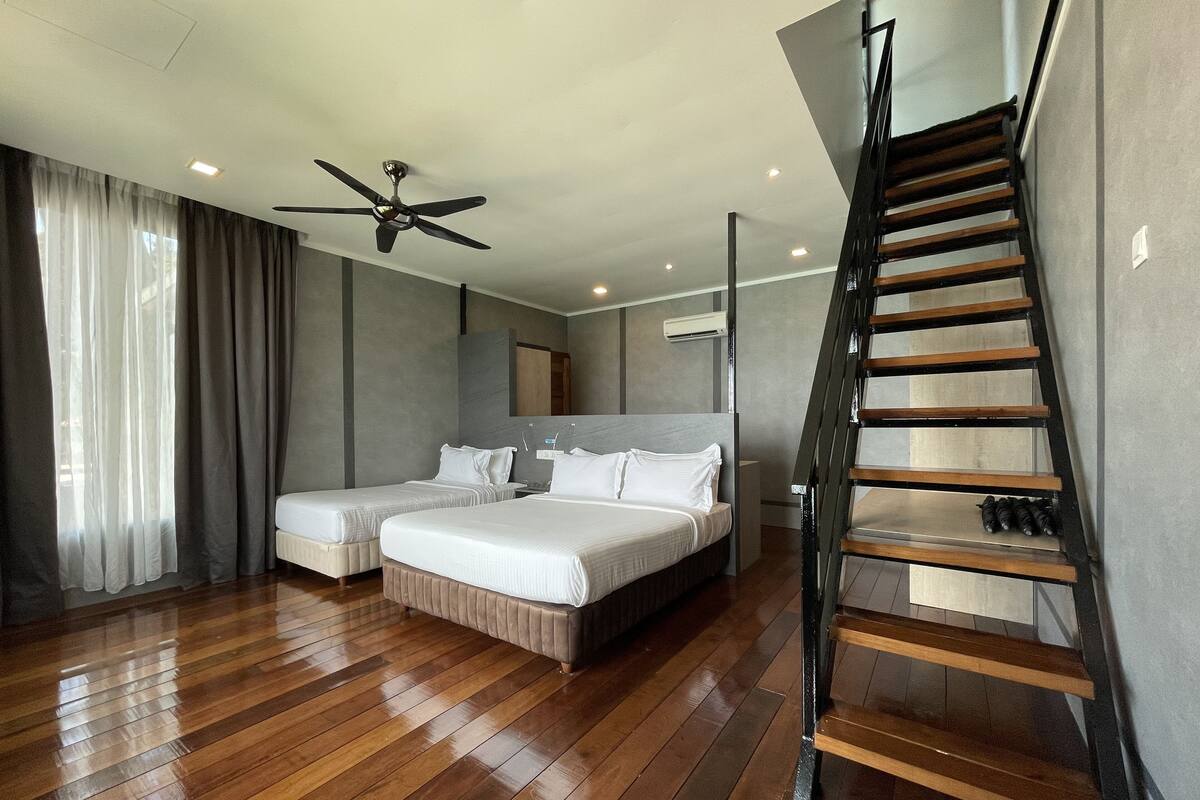 A modern hotel room with two beds, a ceiling fan, a wooden staircase, and a large window with curtains.