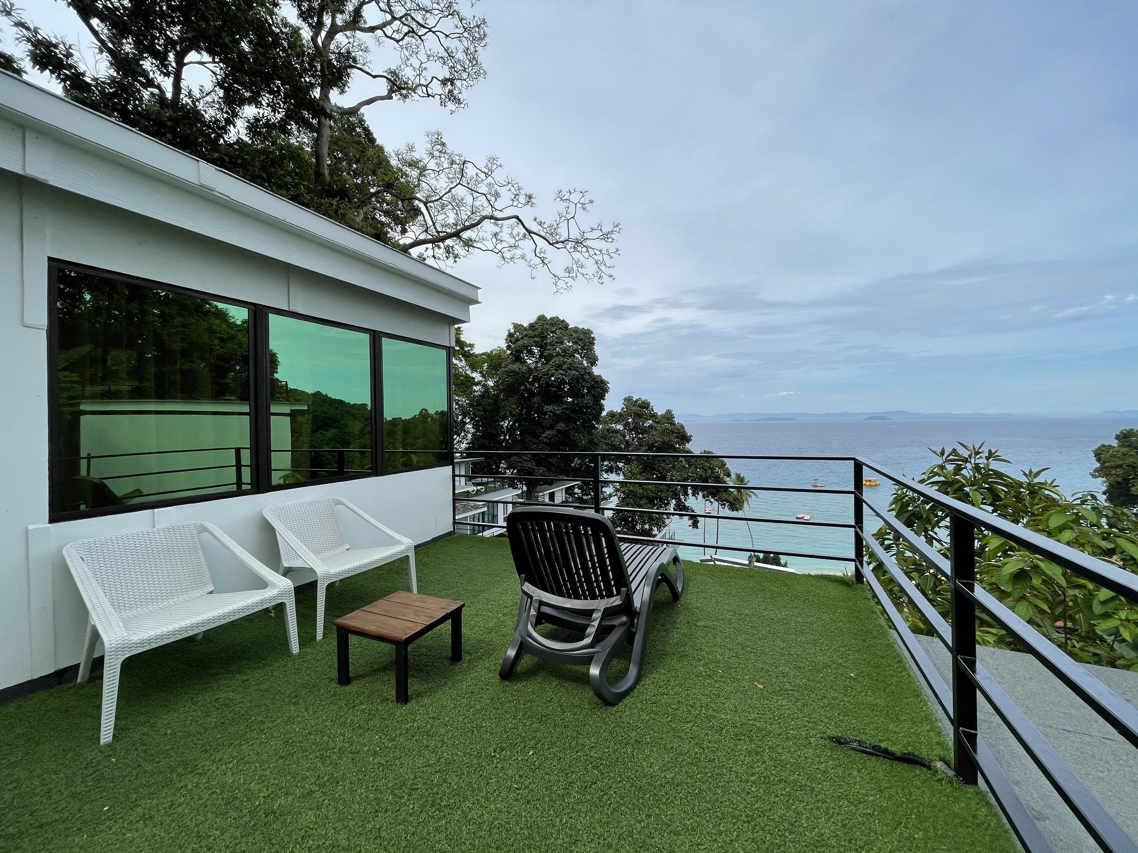 A balcony with artificial grass, two white wicker chairs, a small wooden table, and a black rocking chair.