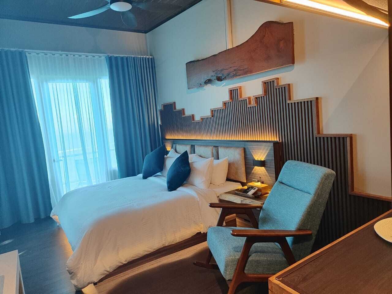 Una habitación de hotel con una cama grande, una zona de estar con una silla y una obra de arte colgada en la pared.