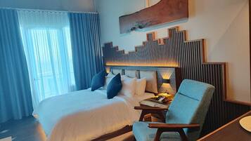 Una habitación de hotel con una cama grande, una zona de estar con una silla y una obra de arte colgada en la pared.