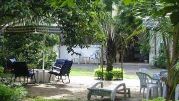 An outdoor seating area with chairs and tables, surrounded by lush greenery and a pergola.