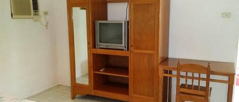 A room with a wooden cabinet containing a television, a chair, and a bed with a floral bedspread.