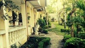 Un chemin de pierre mène à un bâtiment doté d’un balcon, qui est entouré d’une végétation luxuriante et de plantes en pot.