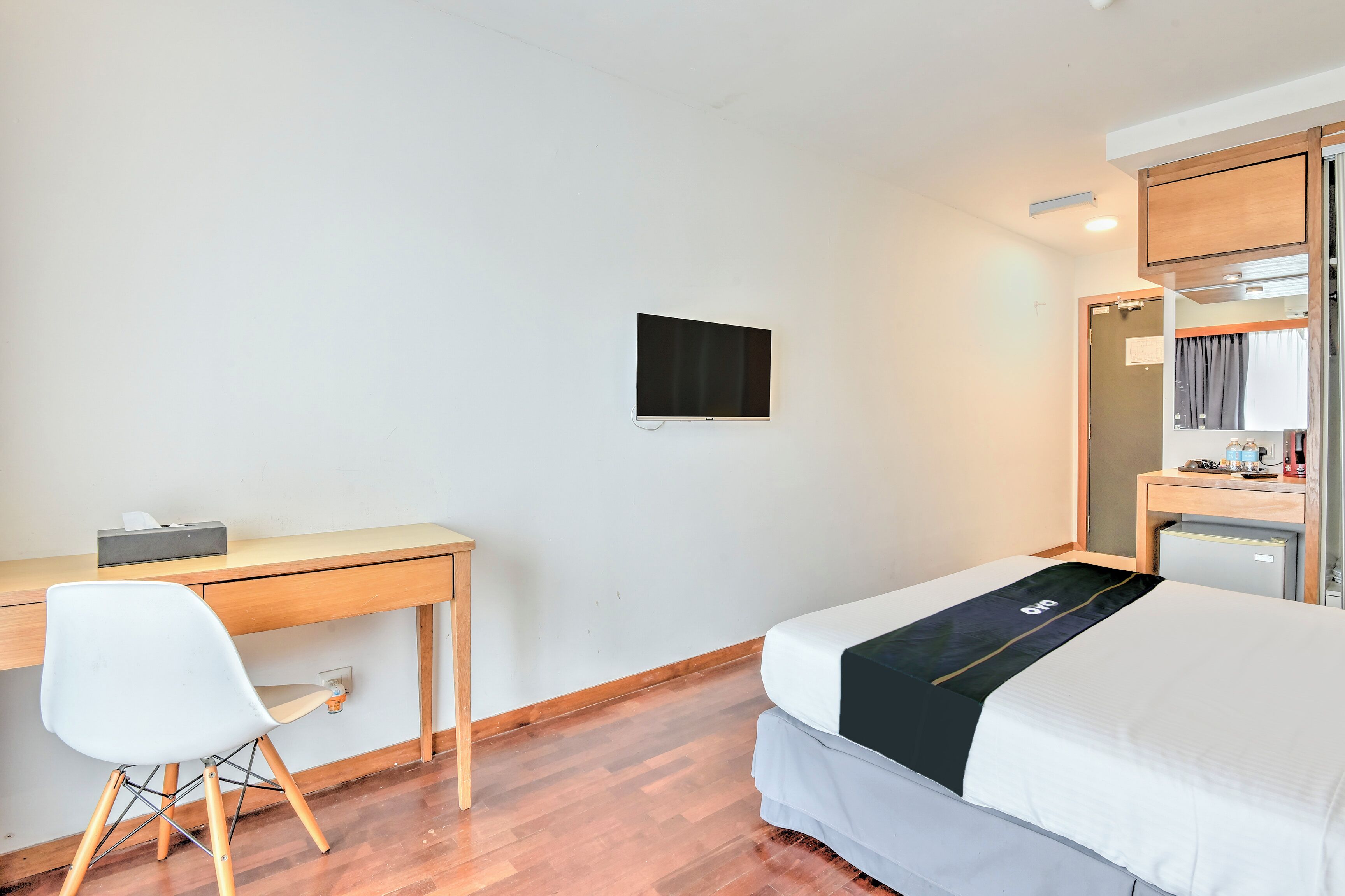 A hotel room with a bed, a desk, a chair, a flat-screen TV, and a small cabinet.