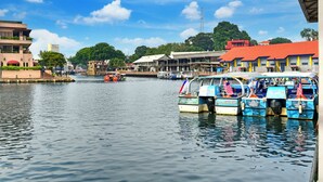 A waterfront area with boats docked, buildings with red roofs, and a clear blue sky. - Sunday Malacca Near Jonker Street Formerly Quayside (Malacca City)