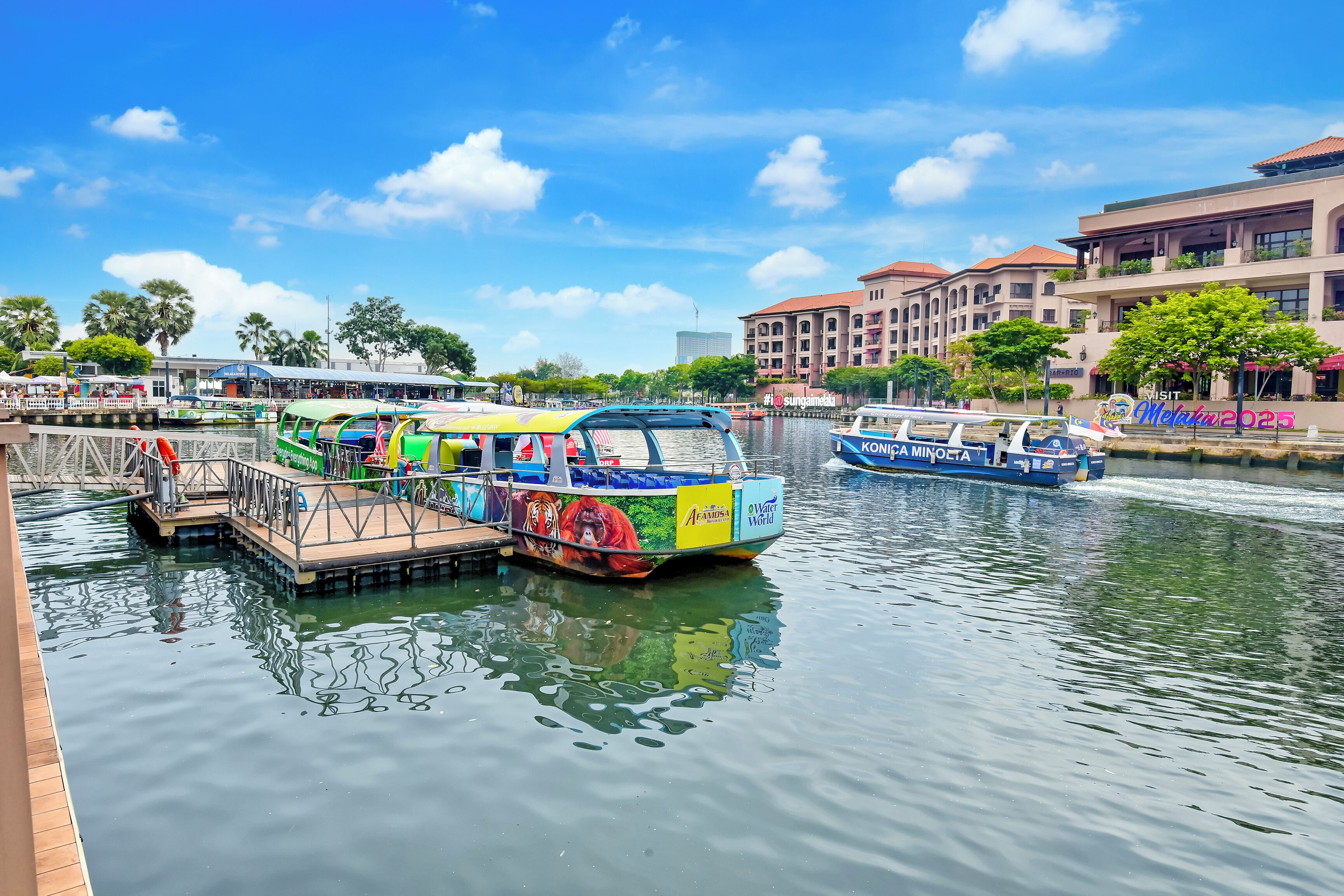 A riverfront with boats docked, a pier, and buildings in the background.