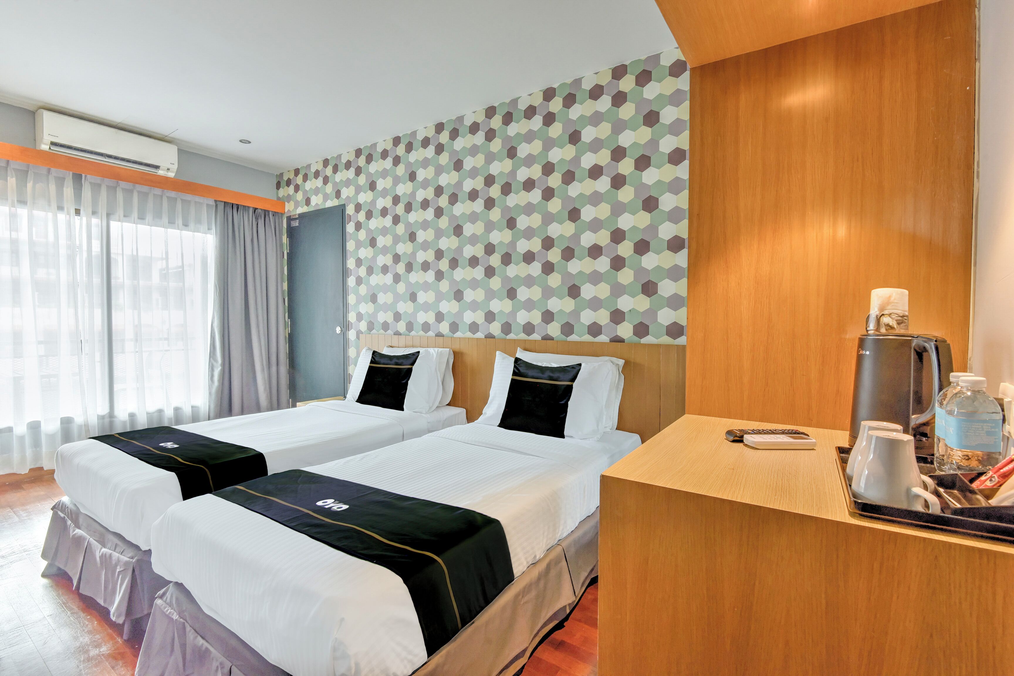 A hotel room with two beds, a wooden desk, a coffee maker, and a patterned wall.