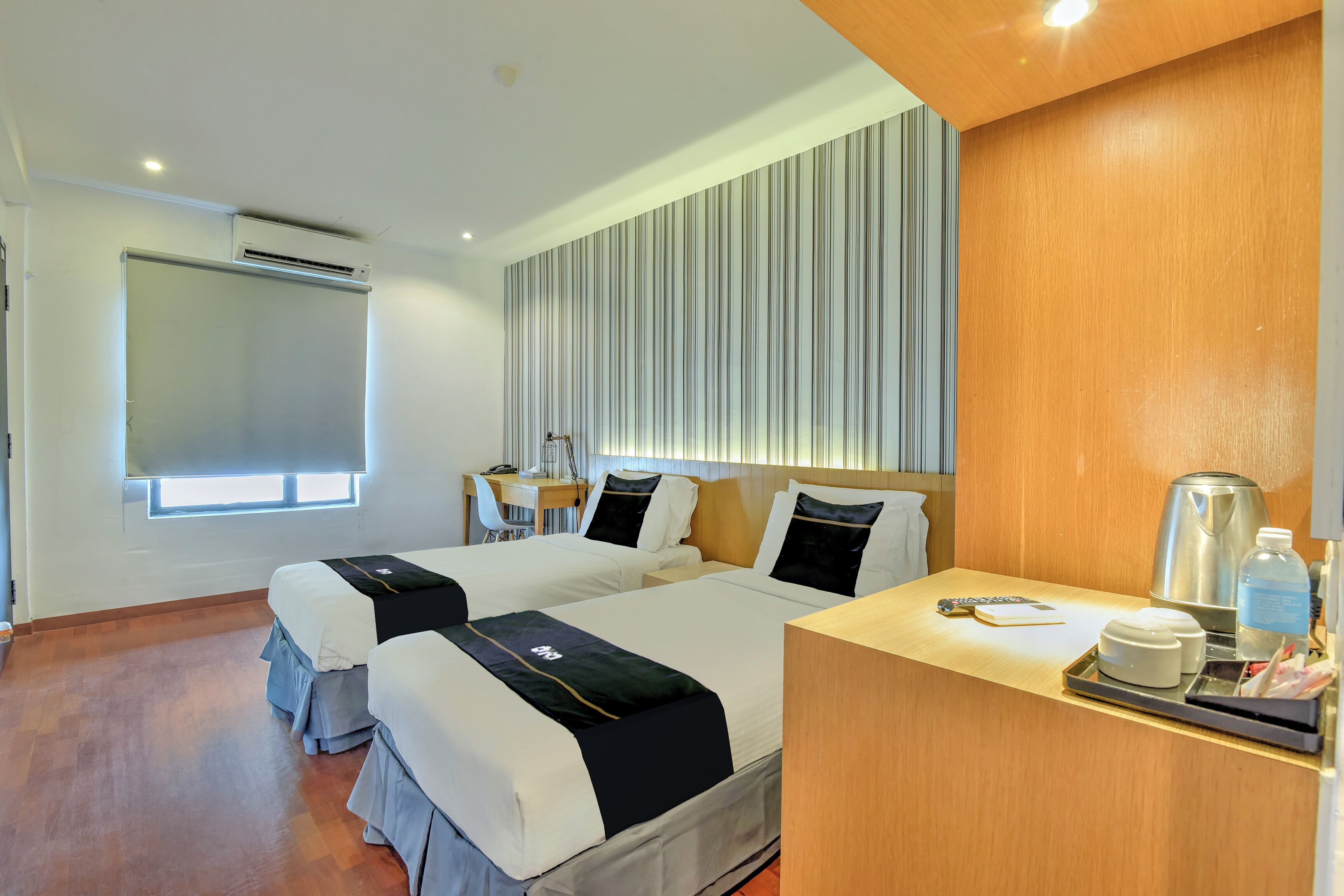 A hotel room with two beds, a desk, a coffee maker, and a window with blinds.