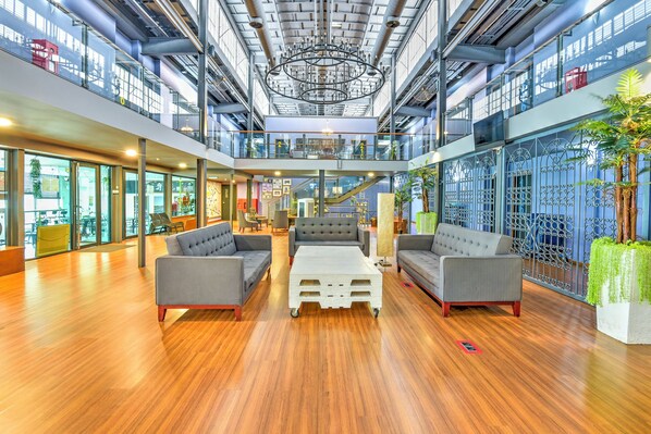 A spacious lobby with high ceilings, a central seating area with sofas and a coffee table, and a view of the city through large windows.