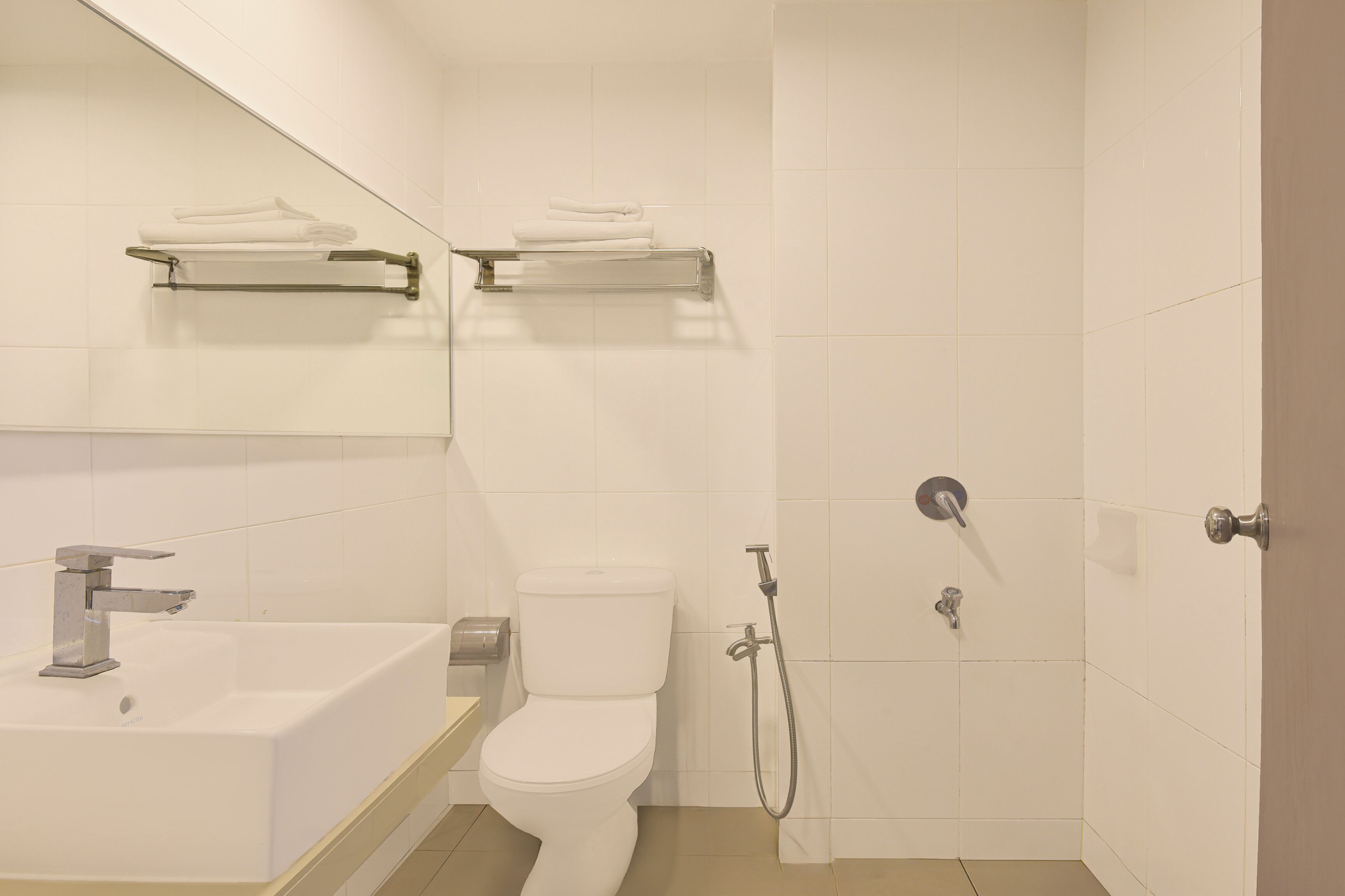 Un baño moderno con lavamanos, inodoro y ducha. Hay toallas en un estante sobre el inodoro.