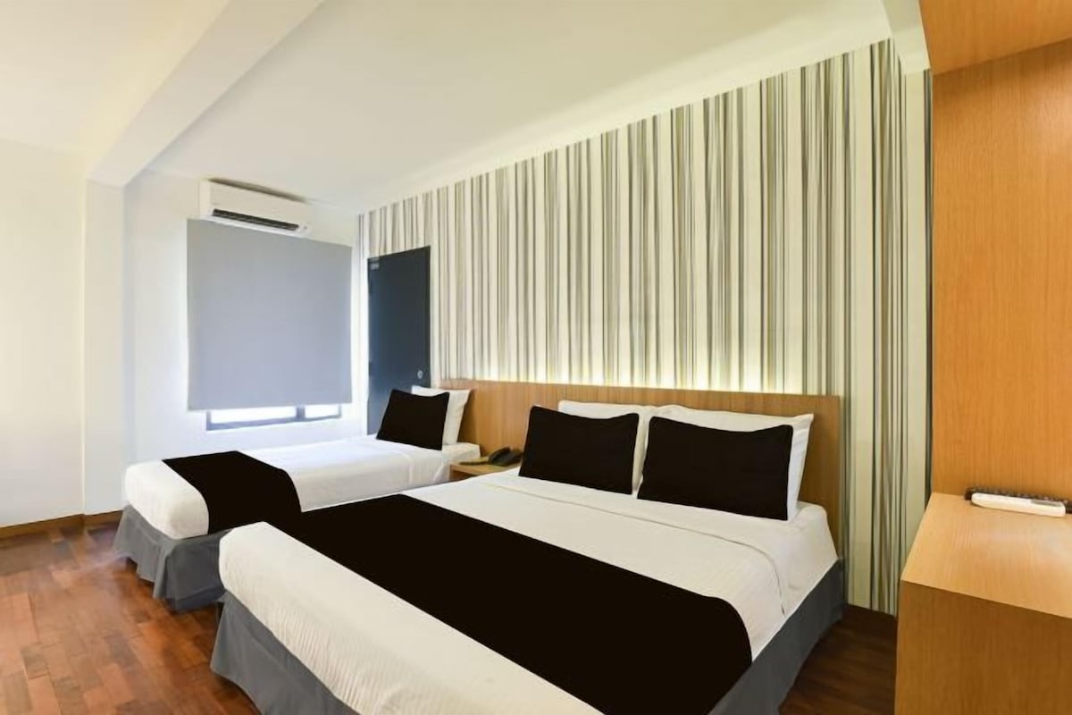 Une chambre d’hôtel avec un grand lit, deux tables de chevet, une armoire et une fenêtre avec des rideaux.