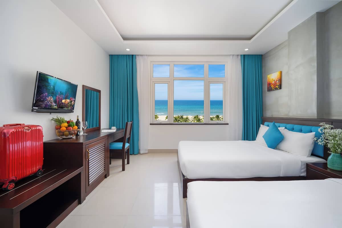 Habitación de hotel con cama, escritorio, televisión y ventana con vista al mar.