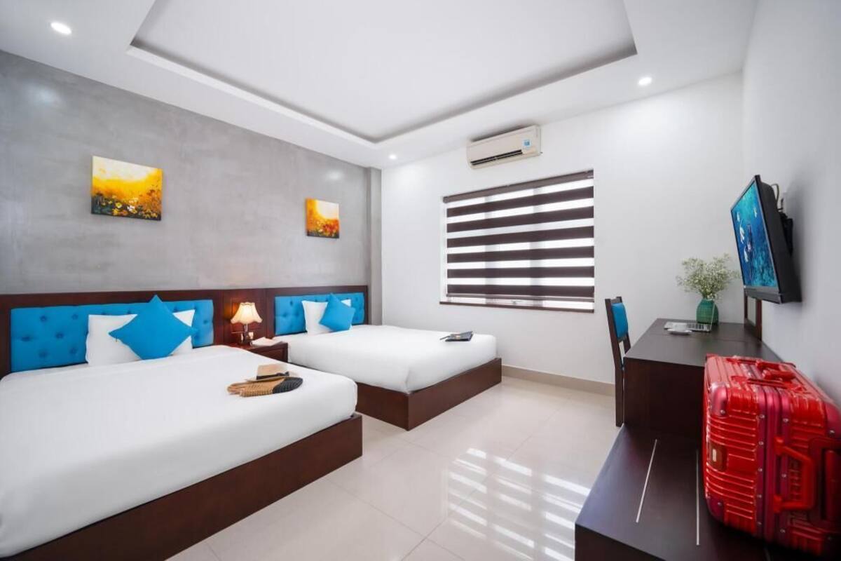 Habitación de hotel con dos camas, un televisor de pantalla plana, un equipo de aire acondicionado y una ventana con persianas.