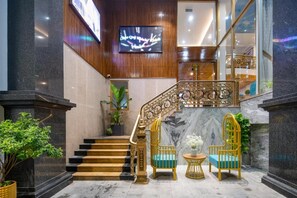 A grand staircase with ornate railings, a marble floor, and a seating area with chairs and a table. - Platinum Beach Hotel (Da Nang)