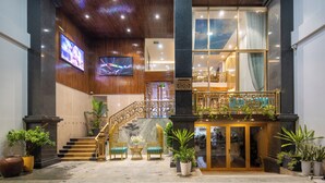 A hotel lobby with a staircase, seating area, and a balcony with plants. - Platinum Beach Hotel (Da Nang)