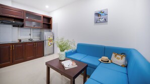 A compact living space with a kitchenette, a blue sofa, a small table, and a decorative vase. - Platinum Beach Hotel (Da Nang)