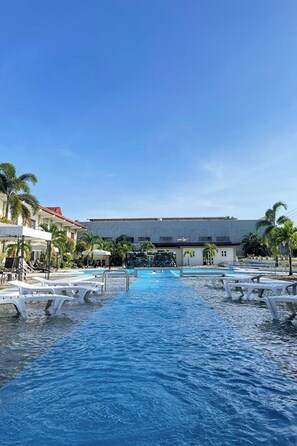 A swimming pool with lounge chairs and palm trees, surrounded by buildings. - Angeles Palace Hotel (Angeles City)