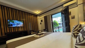 Een hotelkamer met een bed, een televisie aan de muur, een balkon met gordijnen en een wand van hout.