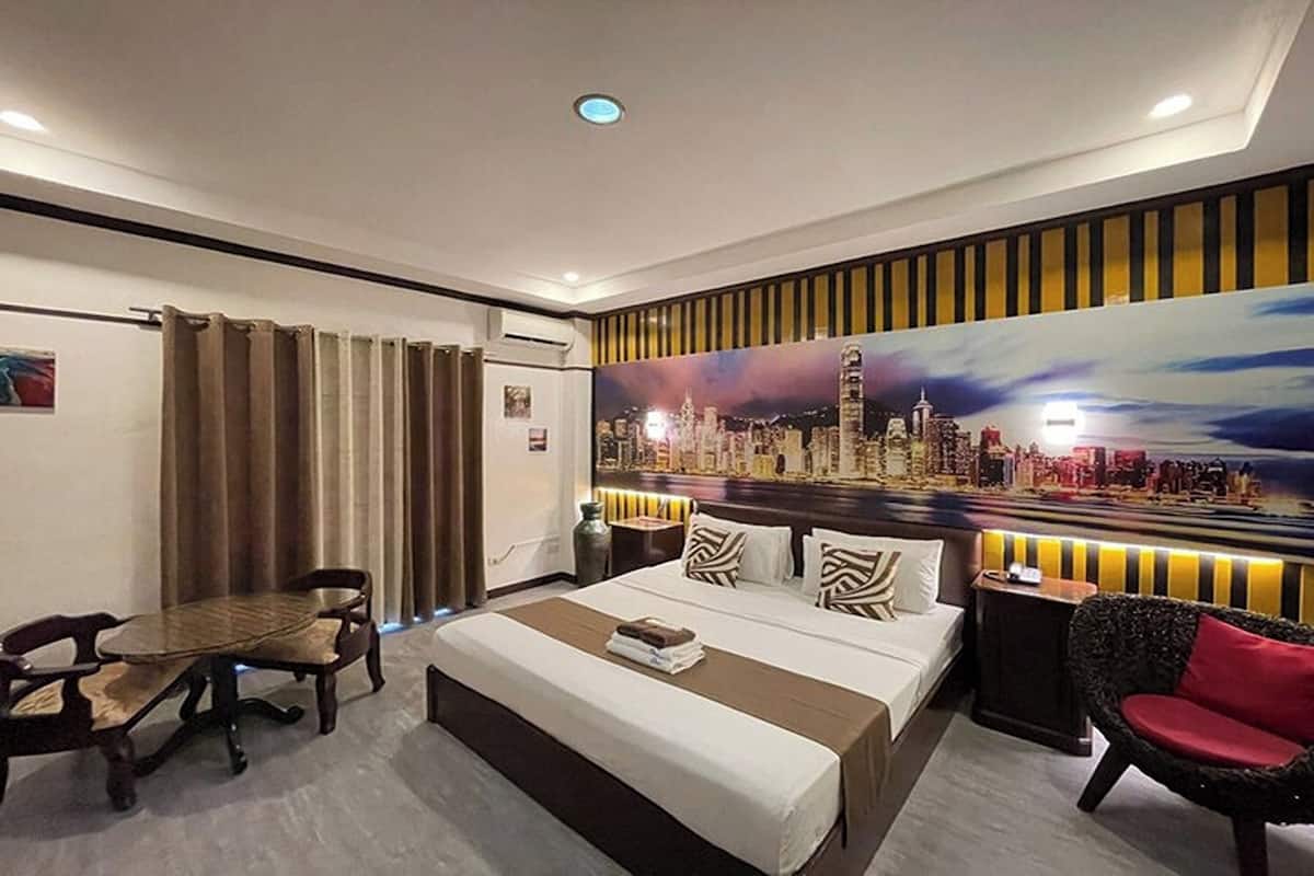 A hotel room with a large bed, a dining table, and a chair. There is a painting of a cityscape on the wall.