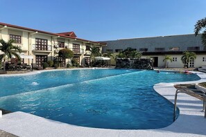 A large outdoor swimming pool with a curved edge, surrounded by a white deck. There are lounge chairs and umbrellas along the poolside. - Angeles Palace Hotel (Angeles City)