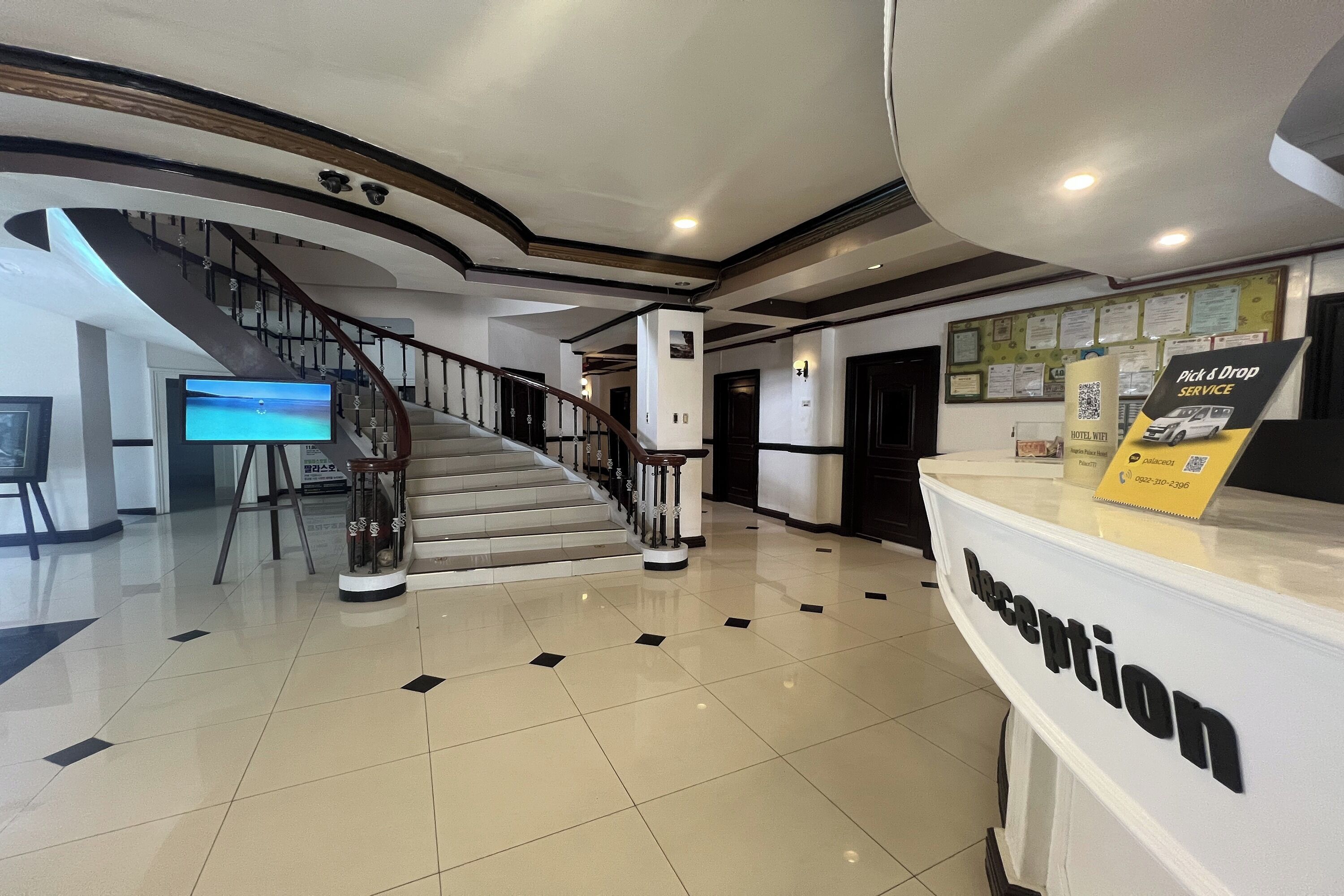 Zona de recepción de un hotel con una escalera moderna, mostrador de recepción y una pantalla digital.