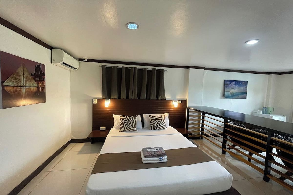 A hotel room with a bed, bedside tables, a desk, and a view of a building.